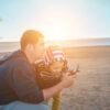 Father and son controlling fly drone on the seashore at sunset in summer day. Freedom, Family, Travel, Journey, Togetherness.