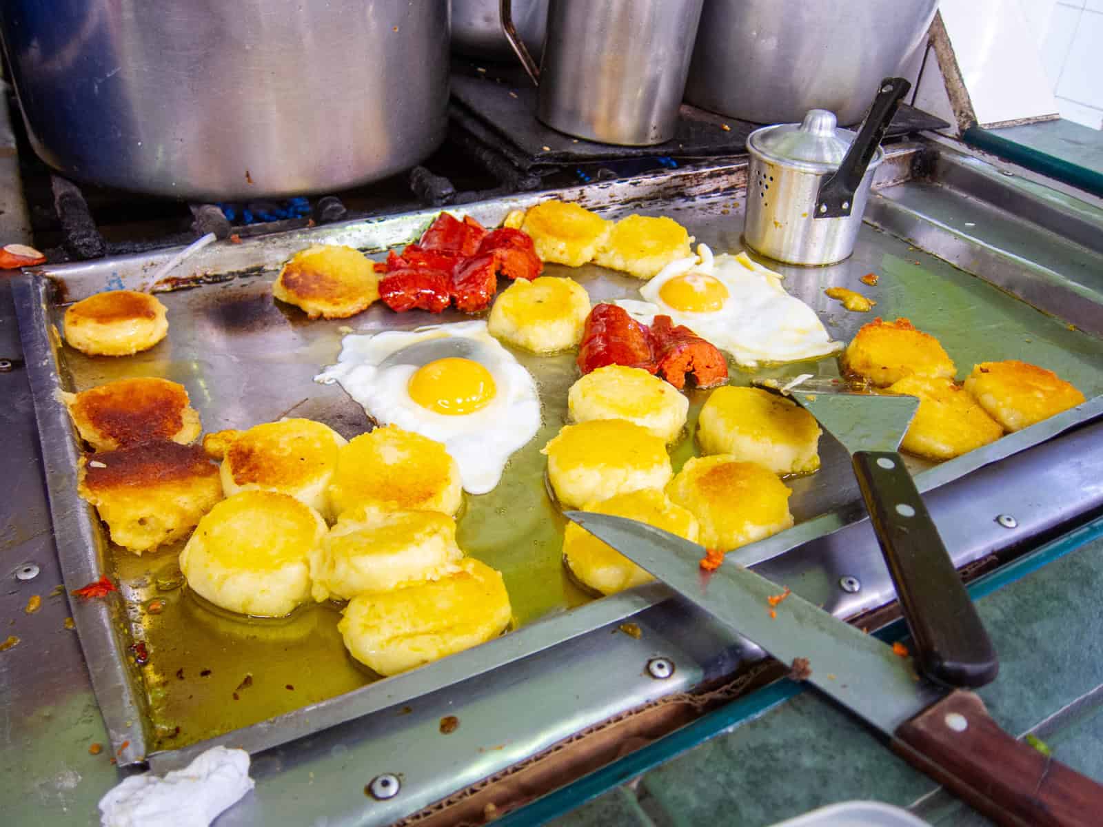 Llapingachos, eggs, and chorizo cooking on a grill at the Market in Banos