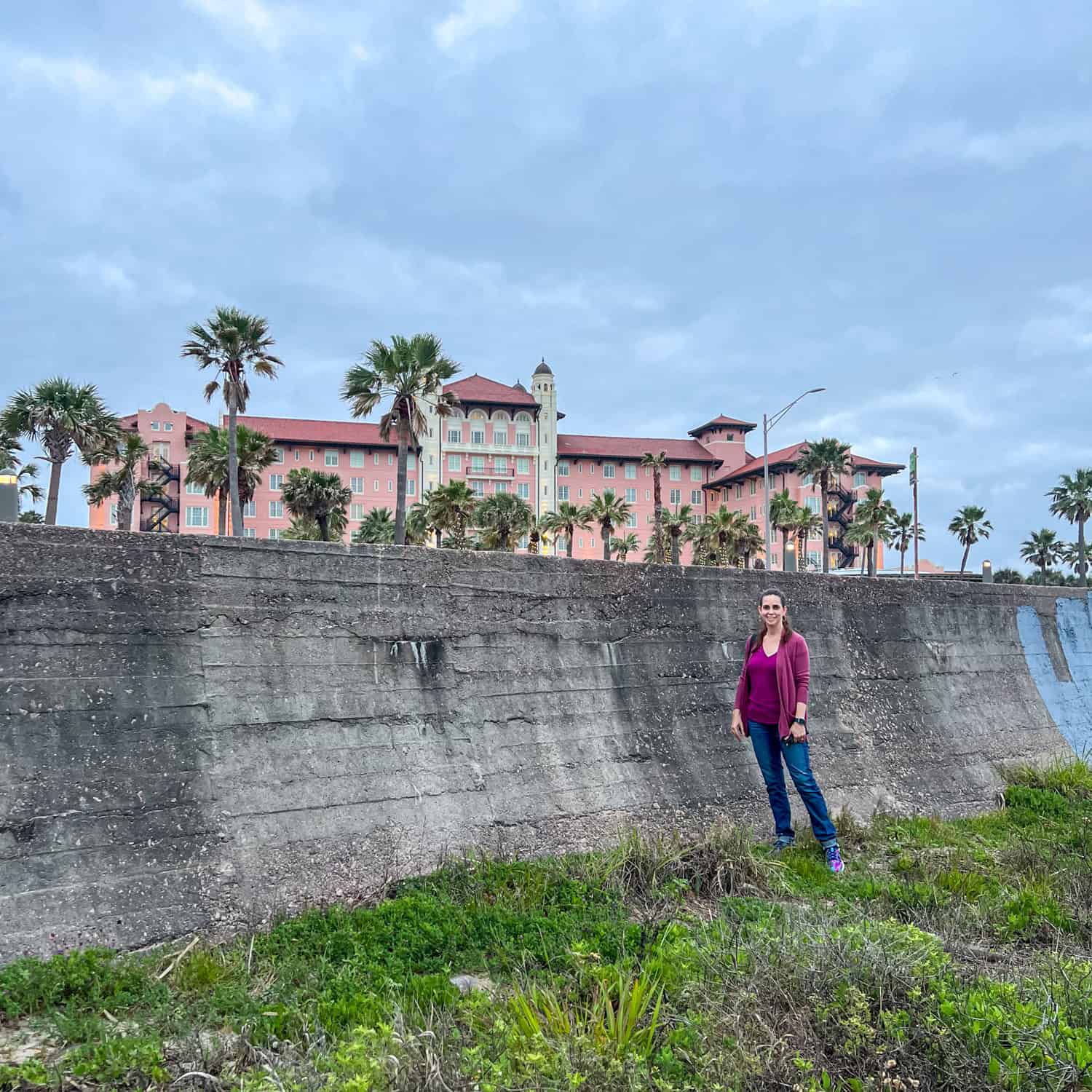 Kel stands on the beach in front of the historic Galveston Seawall, with the Grand Galvez hotel in the background.