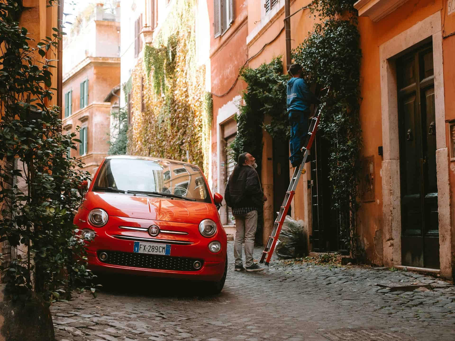 A small red car parked on a narrow street in Trastevere, Rome (photo by Miraxh Tereziu).