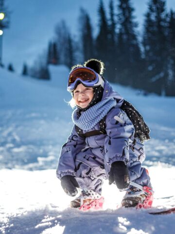 A young girl smiles while snowboarding (photo: Ilya Lisauskas, Pexels).