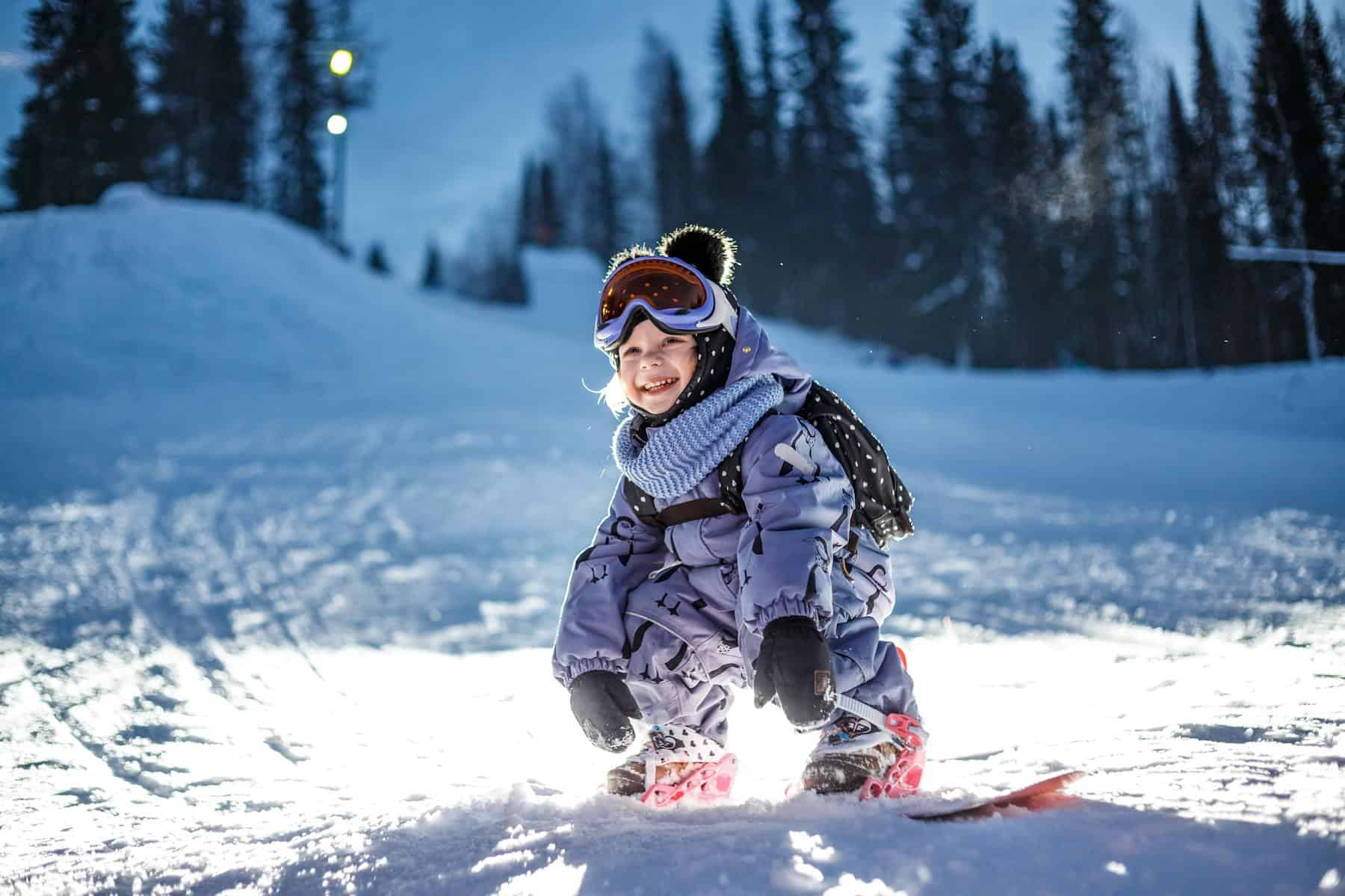 A young girl smiles while snowboarding (photo: Ilya Lisauskas, Pexels).