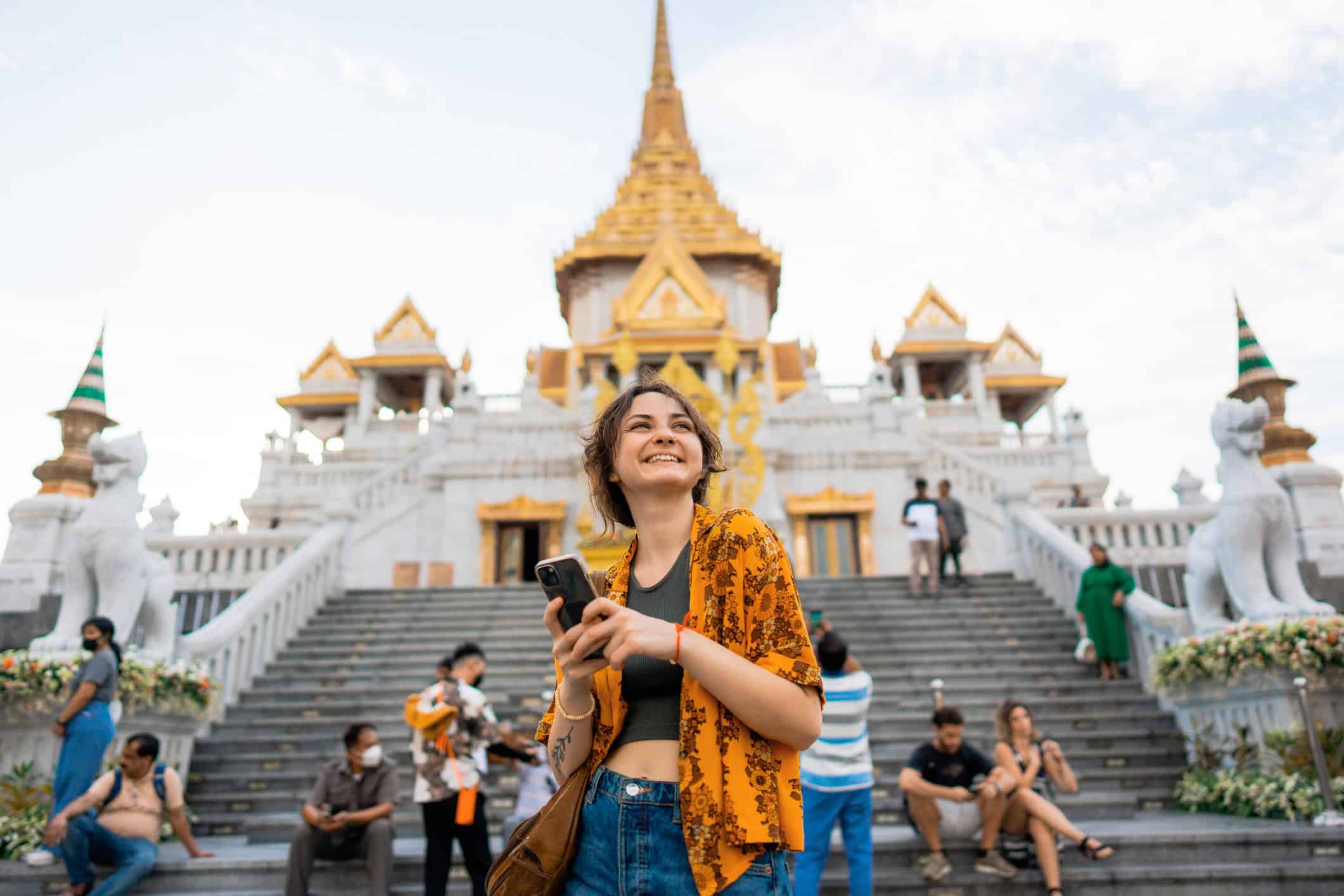 A woman using an eSIM with her phone at Wat Traimit in Bangkok, Asia (photo: Oleh Slobodeniuk, iStock).
