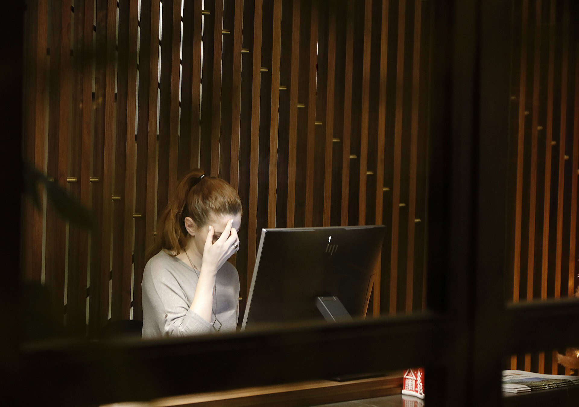 A woman stressed at work in front of a computer monitor (photo by Vasilis Caravitis, Unsplash).