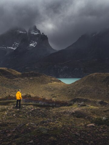 A hiker in a yellow jacket under dark storm clouds in Torres del Paine National Park, Argentina (photo: Andrew Svk, Unsplash).