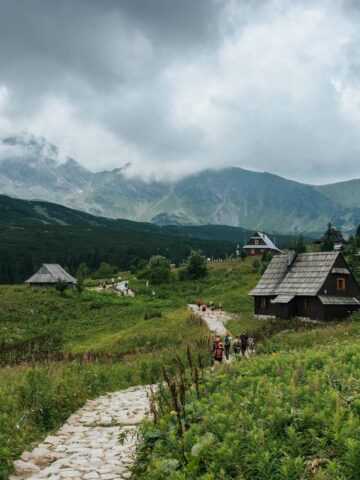 Hikers walking a stone trail past traditional wooden huts in the Tatra Mountains near Zakopane, Poland (photo: Pexels).