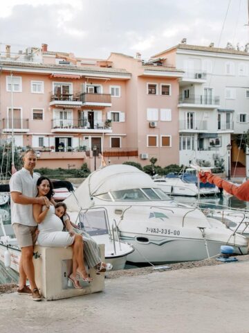 Maternity photoshoot in Valencia at Marina Port Saplaya with family posing by boats and colorful waterfront houses.
