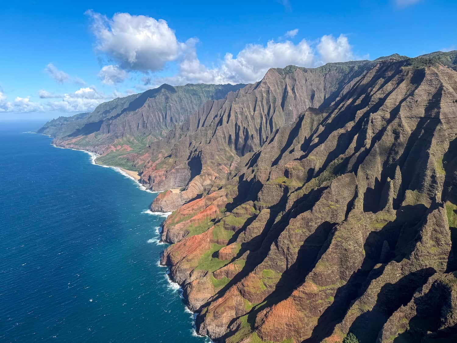 Aerial view of the Na Pali Coast on Kauai with red and green sea cliffs rising above the Pacific Ocean