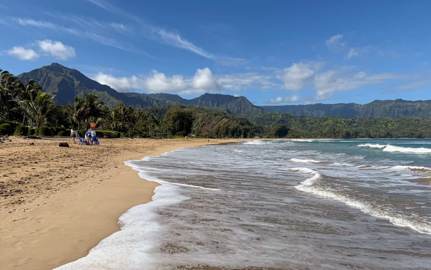 Hanalei Bay beach on Kauai with gentle waves, golden sand, and green mountains in the background