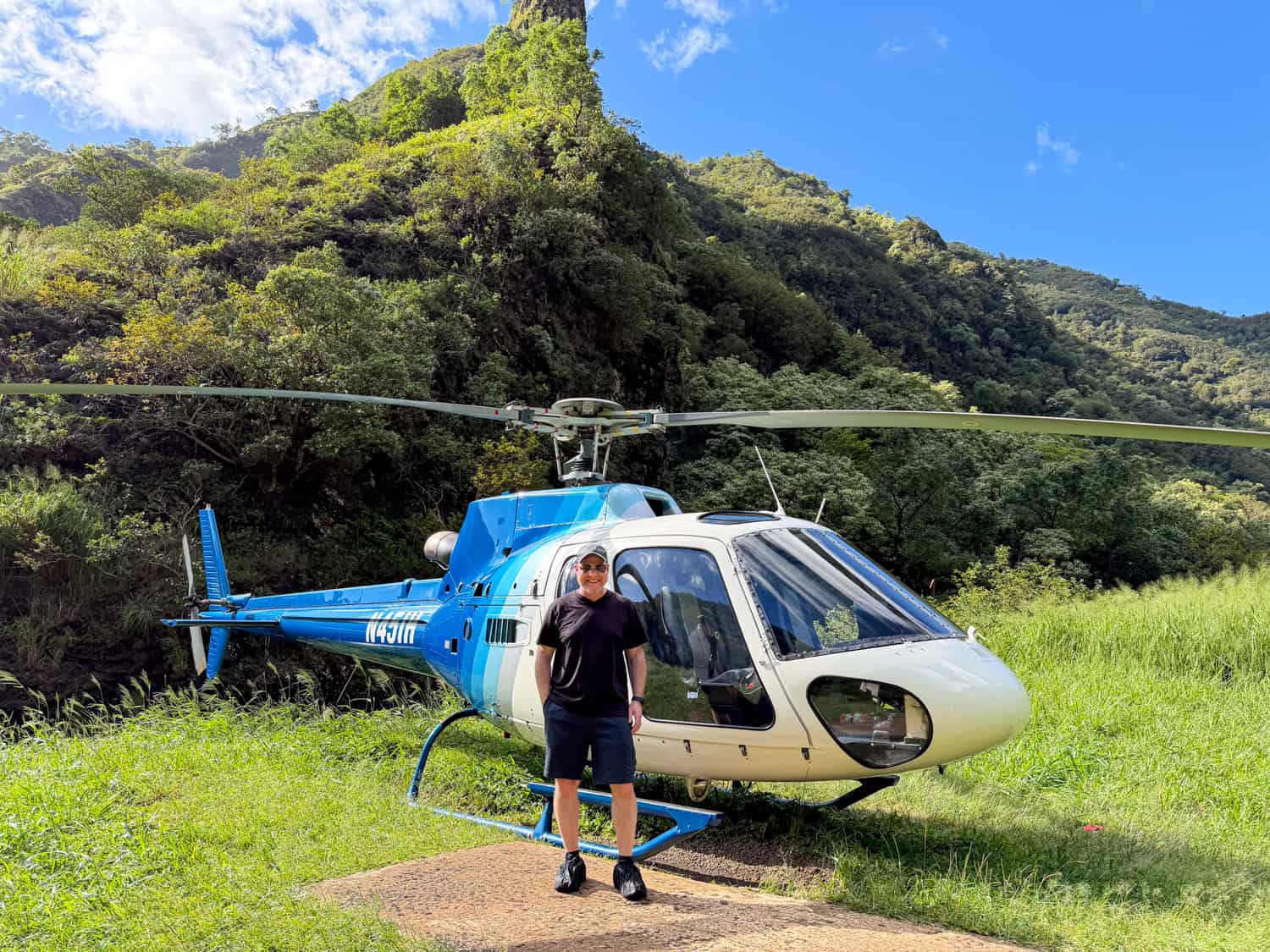 The author standing beside a blue helicopter in a lush green valley on a Kauai helicopter tour