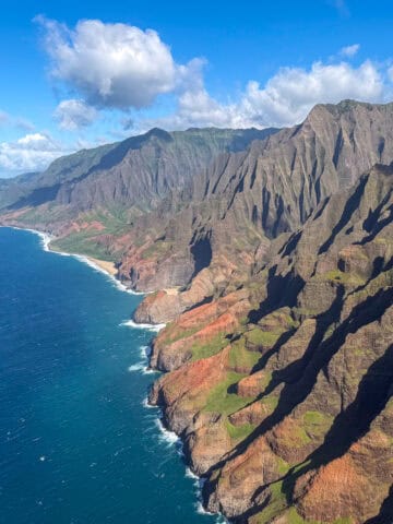 Aerial view of the Na Pali Coast on Kauai with red and green sea cliffs rising above the Pacific Ocean