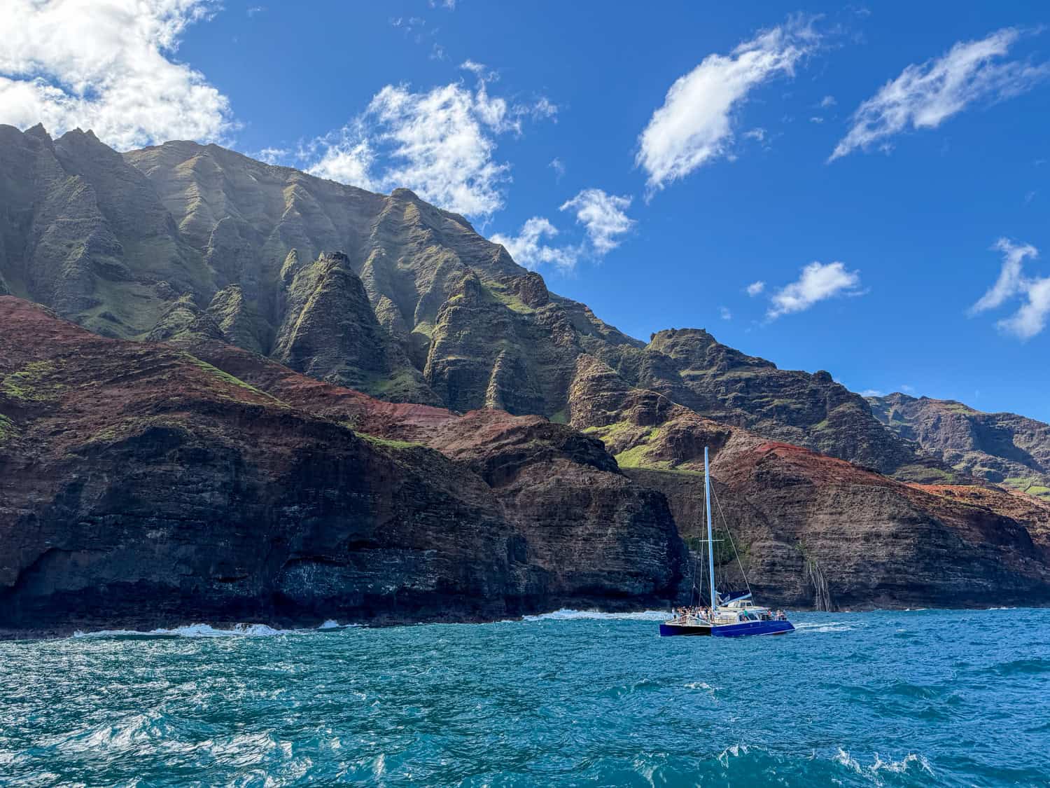 Catamaran sailing along the Na Pali Coast cliffs on Kauai with turquoise ocean water and steep sea cliffs