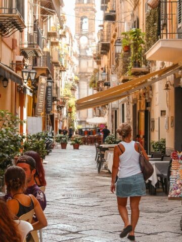 Pedestrians and outdoor cafes along a narrow street in Palermo, Italy