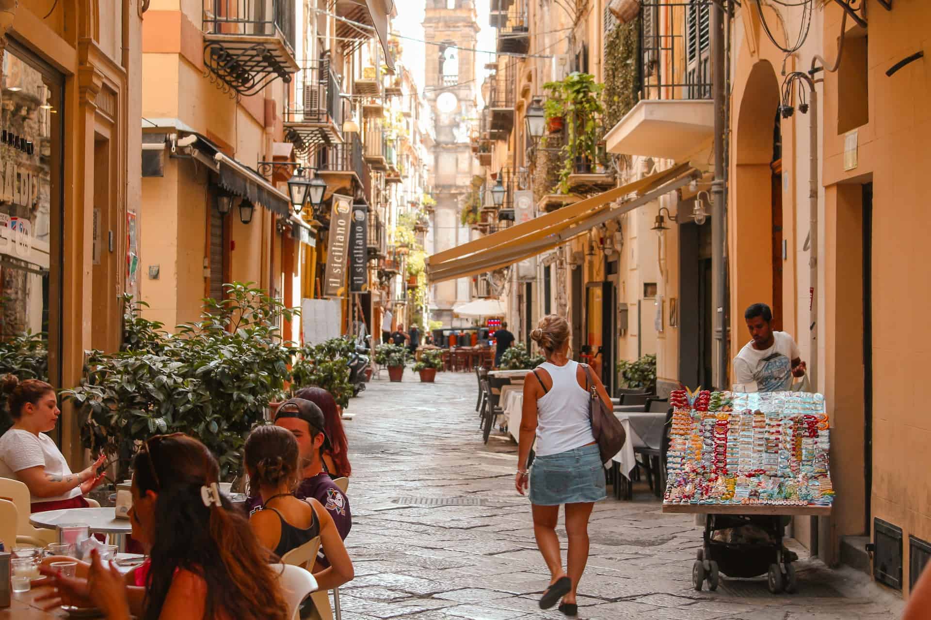 Pedestrians and outdoor cafes along a narrow street in Palermo, Italy
