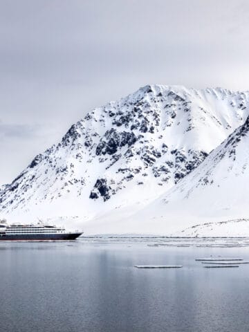 Cruise ship sailing beneath snow-covered mountains in a Svalbard fjord