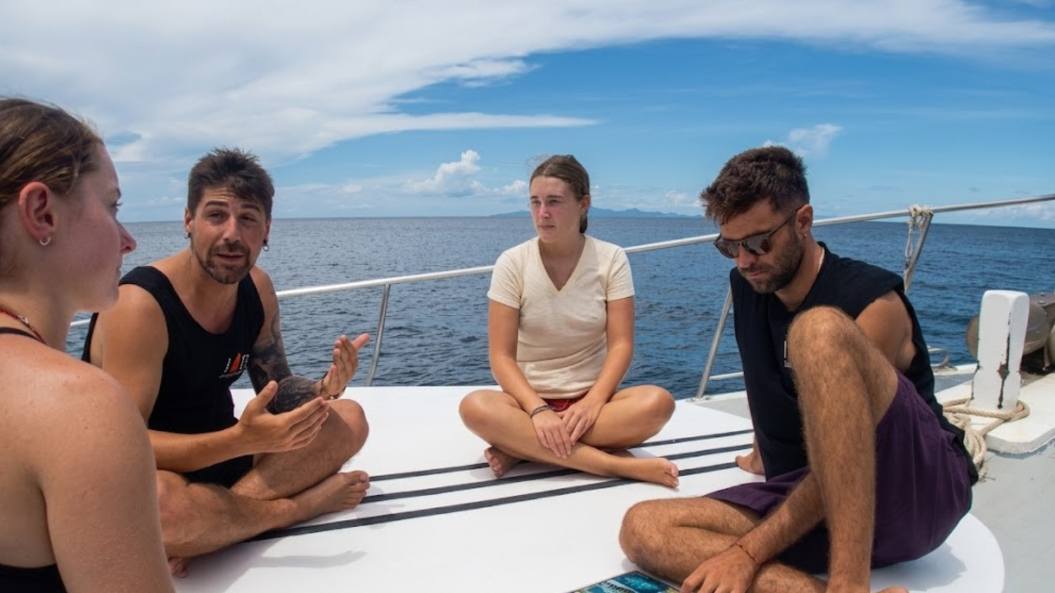 Dive instructor speaking with three students on the deck of a boat in Koh Tao.