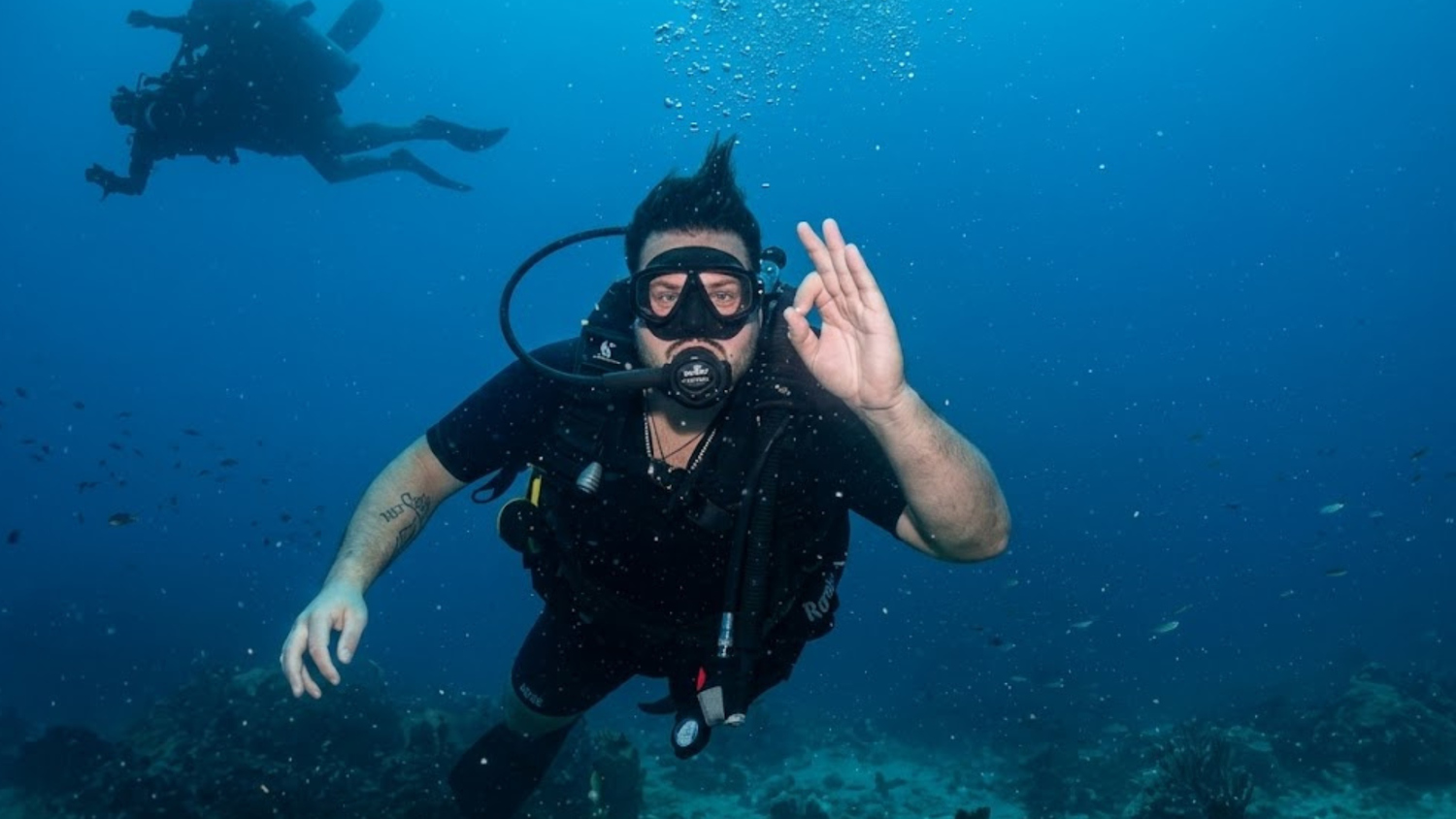 Scuba diver giving the OK hand signal underwater near a coral reef in Koh Tao.