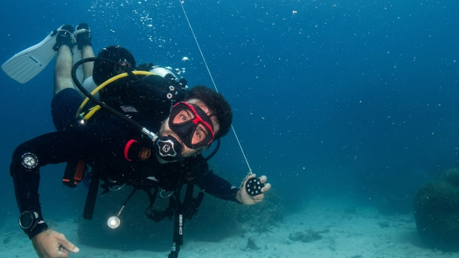 Two scuba divers underwater beside a descent line above the seabed in Koh Tao.