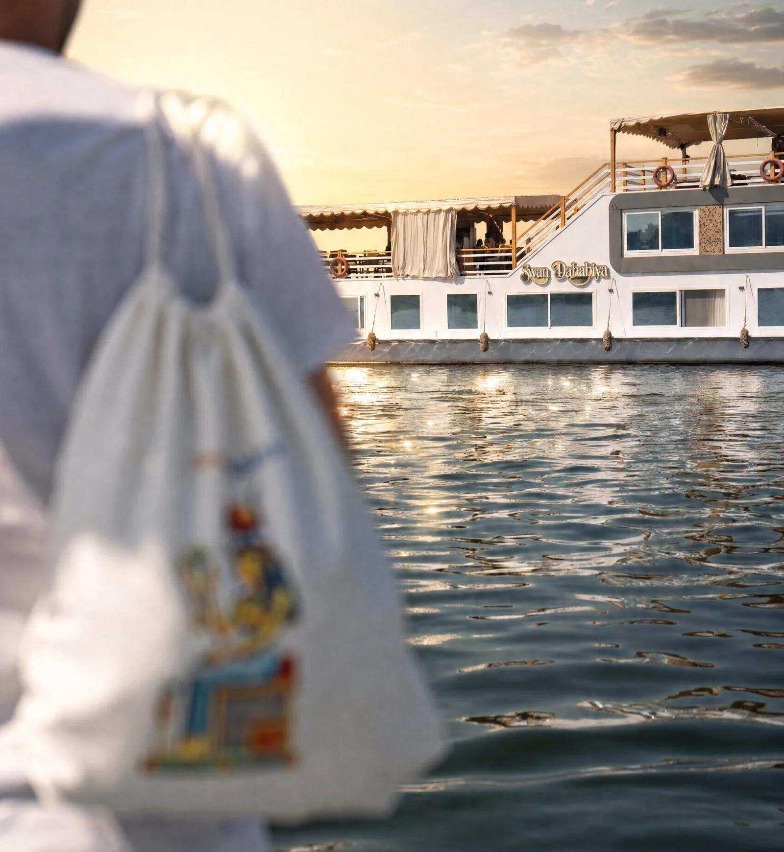 Swan Dahabiya on the Nile at sunset, viewed past a person in white
