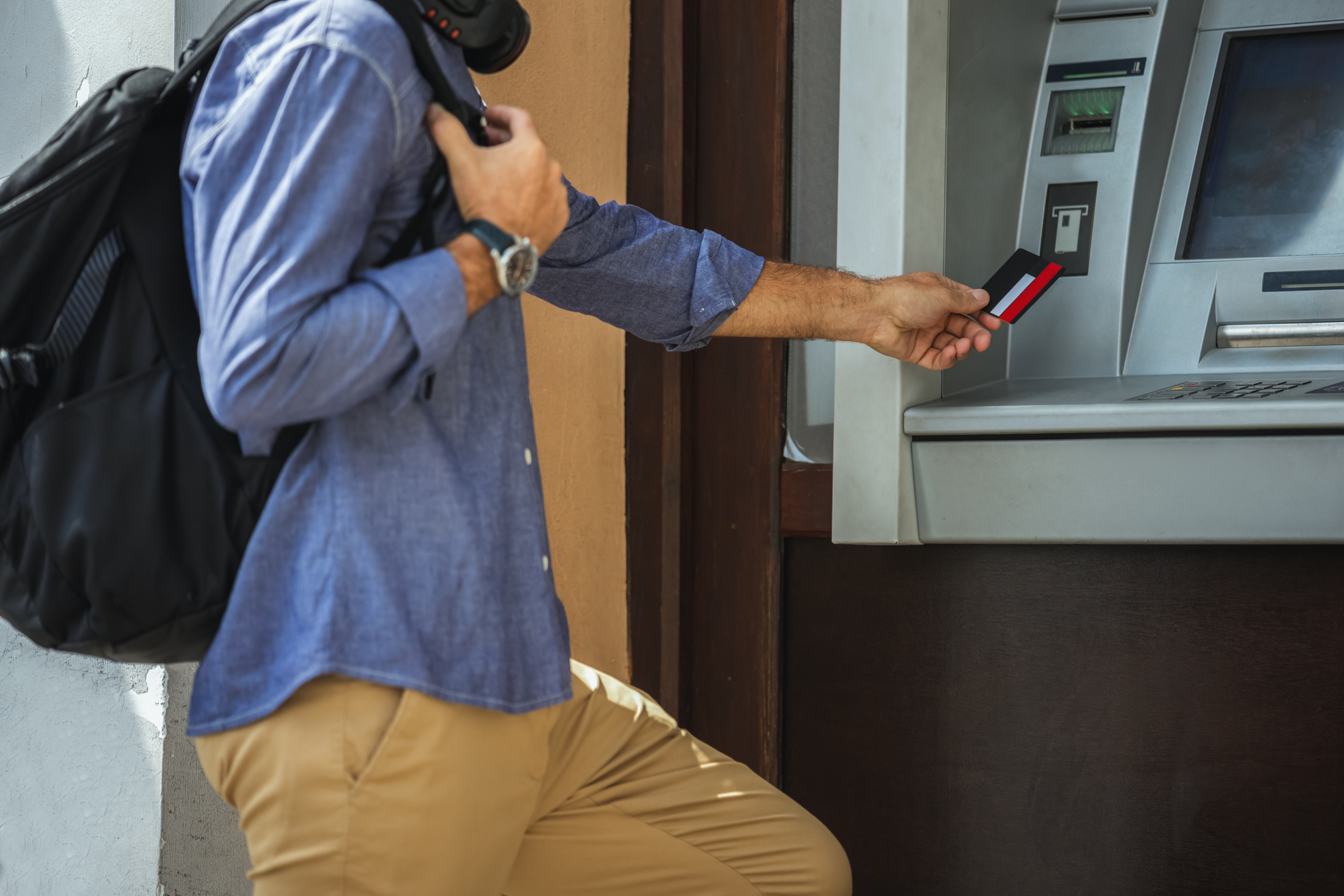 Traveler with a backpack using a bank card at an ATM abroad