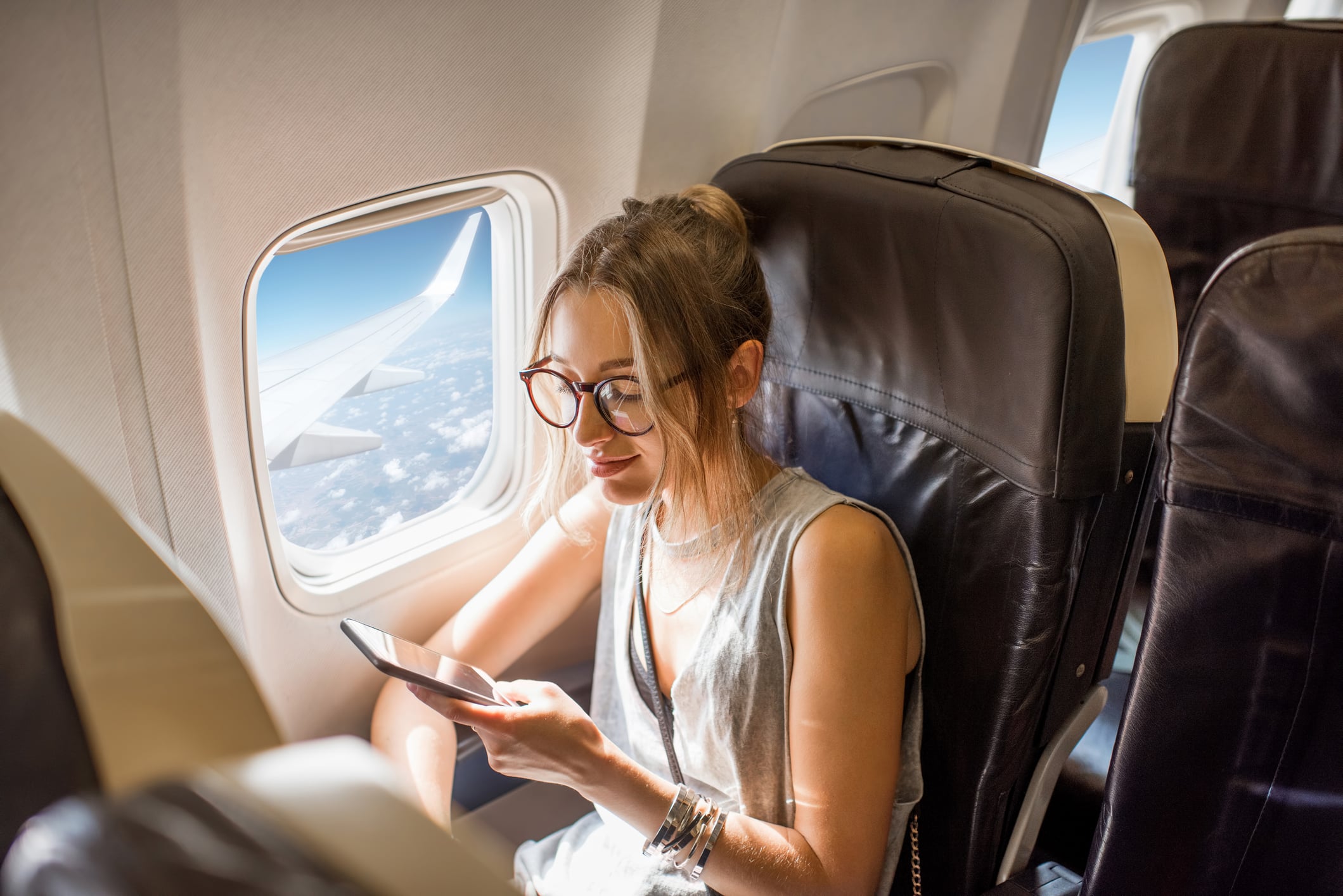 Traveler using a smartphone beside an airplane window on a long flight