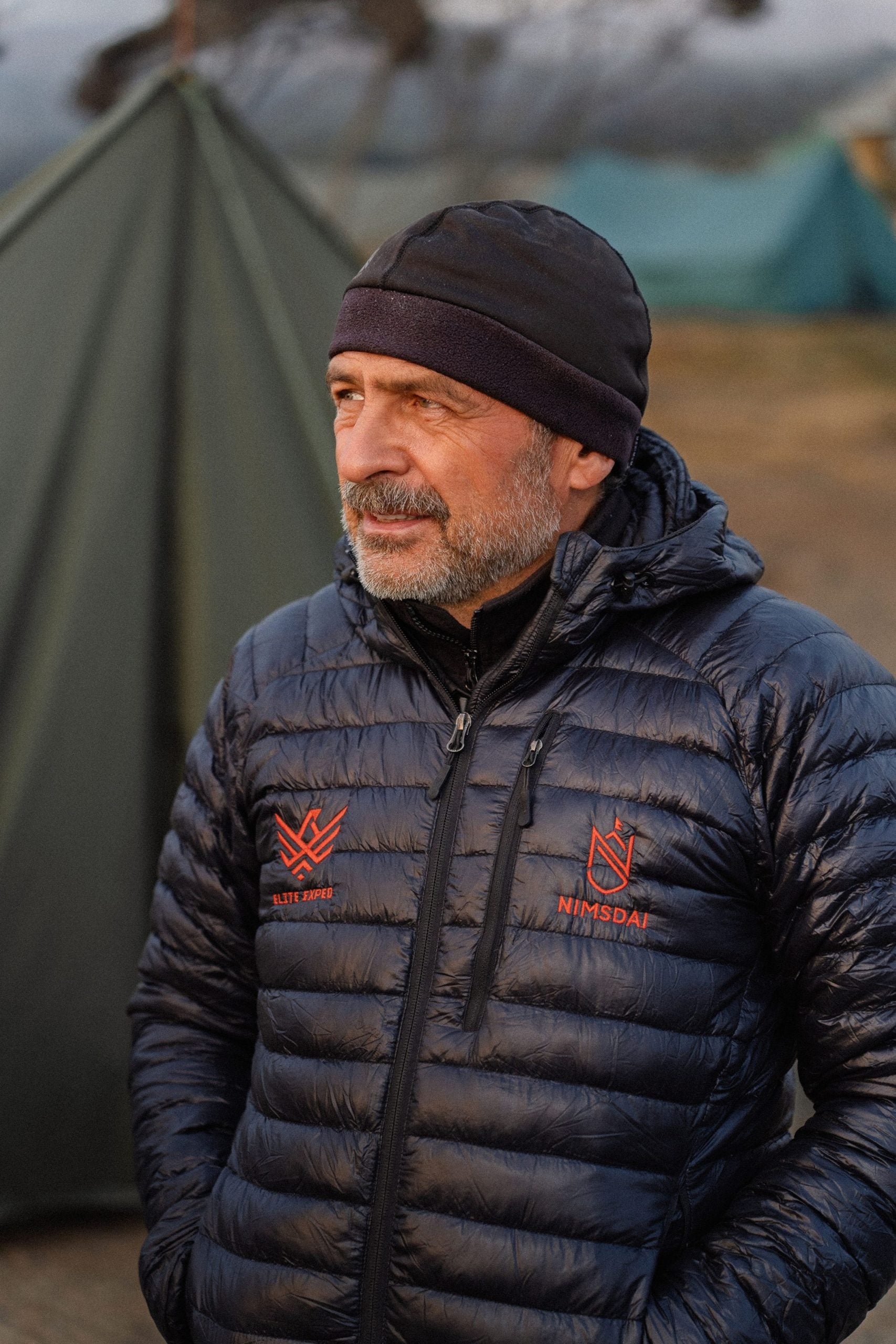 Yevgen Staroselskiy wearing a black beanie and down jacket in front of expedition tents.