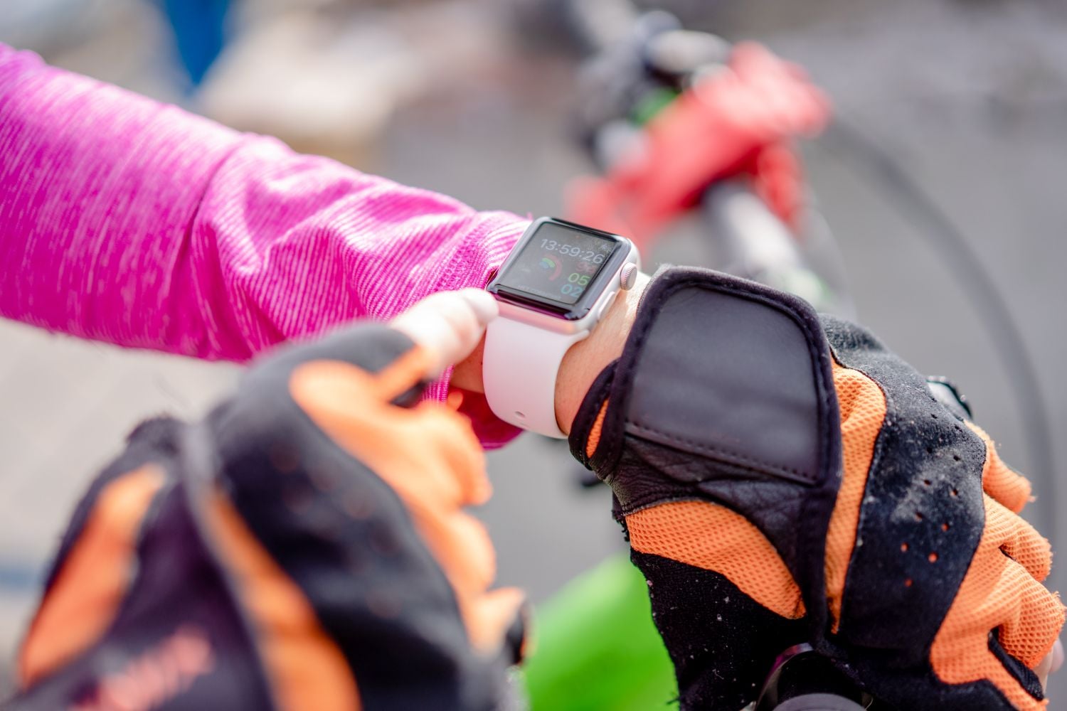 Cyclist wearing orange-and-black gloves checks an Apple Watch with a pale pink band.