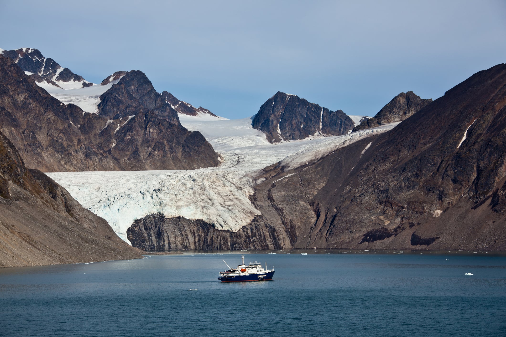 Small expedition ship in Svalbard's Krossfjord beneath a glacier and jagged mountains.