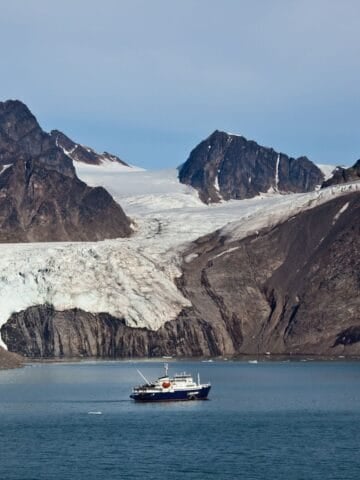Expedition ship in Svalbard's Krossfjord beneath a glacier and mountains.